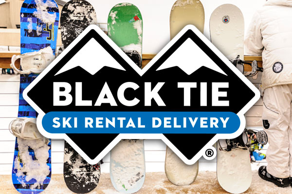 black tie ski rental delivery logo foreground five snowboards leaning against fence background