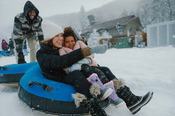 Mom hugging her little girl while sitting on a snow tubing tube while Dad pushes them from behind