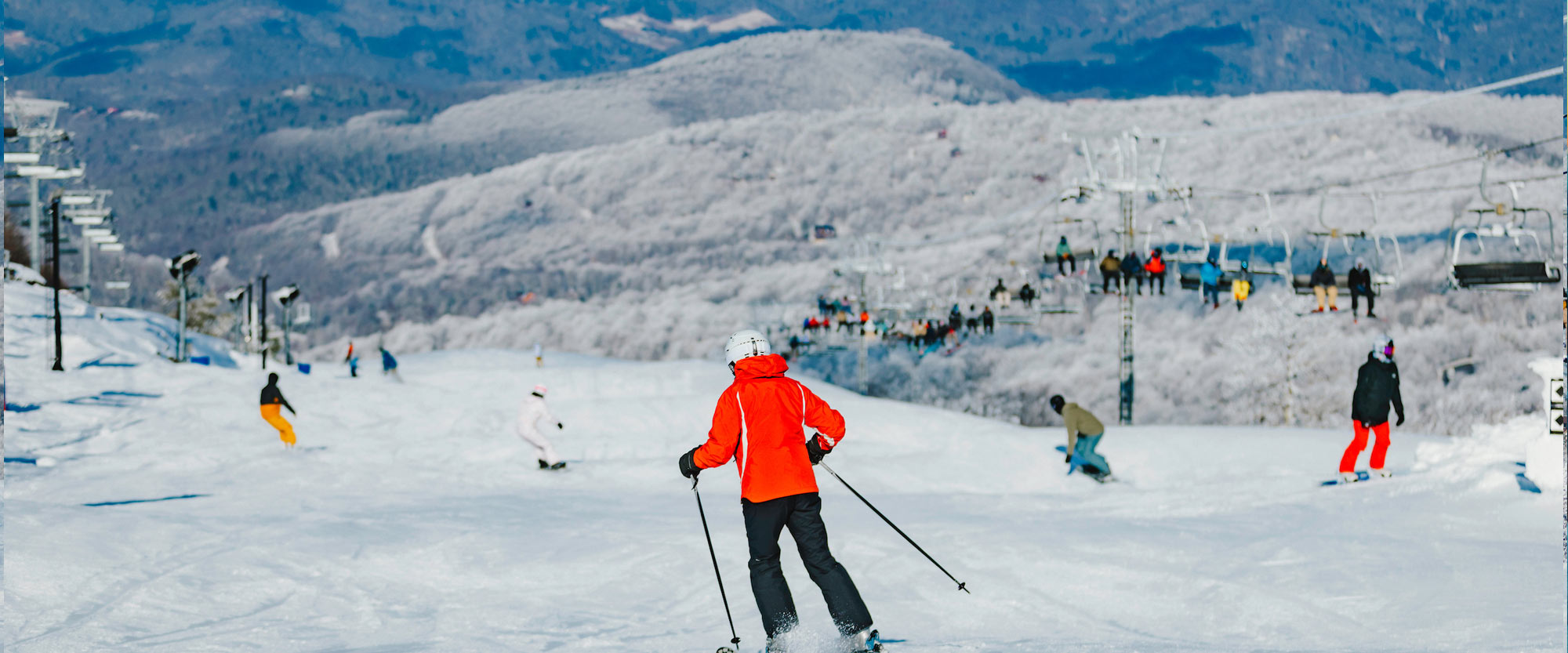 Skiers on the slopes of the Beech Mountain Resort with snow covered peaks in the background